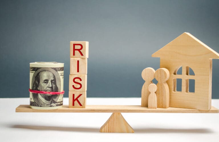 What is the average cost of earthquake insurance. Wooden house and cubes with the word risk and family stand on scales. The concept of risk, loss of real estate. Property insurance. Loans secured by home, apartment. Financial risks, litigation.