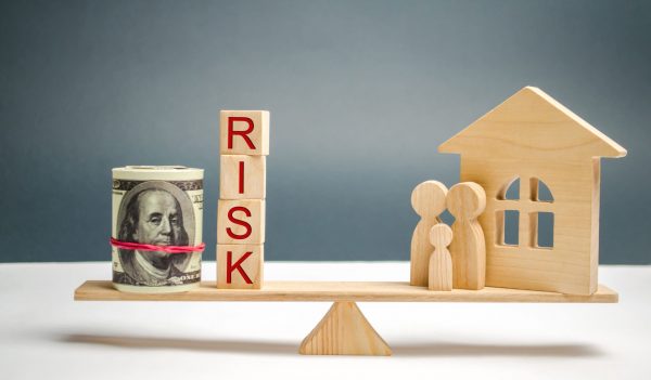 What is the average cost of earthquake insurance. Wooden house and cubes with the word risk and family stand on scales. The concept of risk, loss of real estate. Property insurance. Loans secured by home, apartment. Financial risks, litigation.